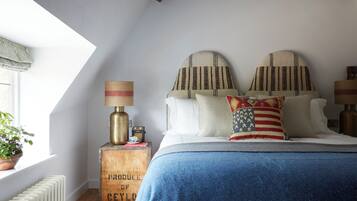 A bedroom with a sloped ceiling, a bed with a blue blanket, patterned pillows, a lamp, and a radiator.