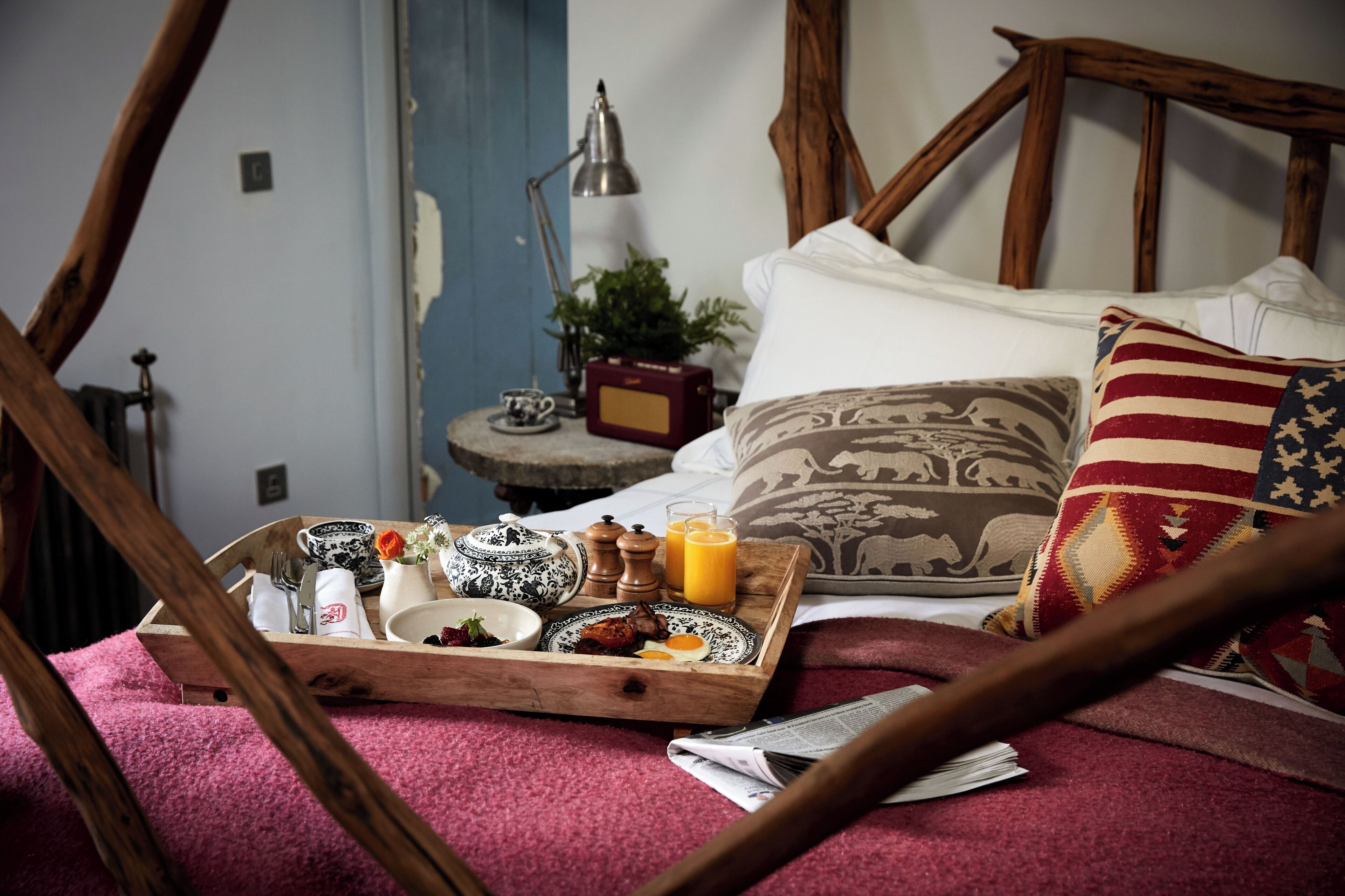 A bed with a wooden headboard, a tray with breakfast items, a lamp, and a plant on a bedside table.