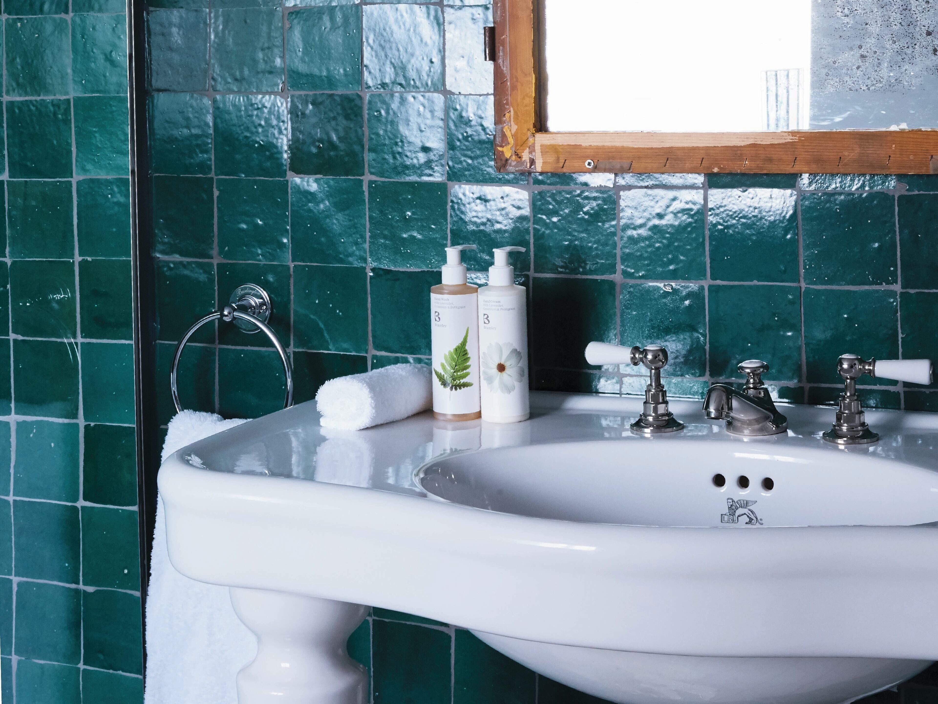 A bathroom with a white sink, green tiles, a window, and two bottles of lotion.