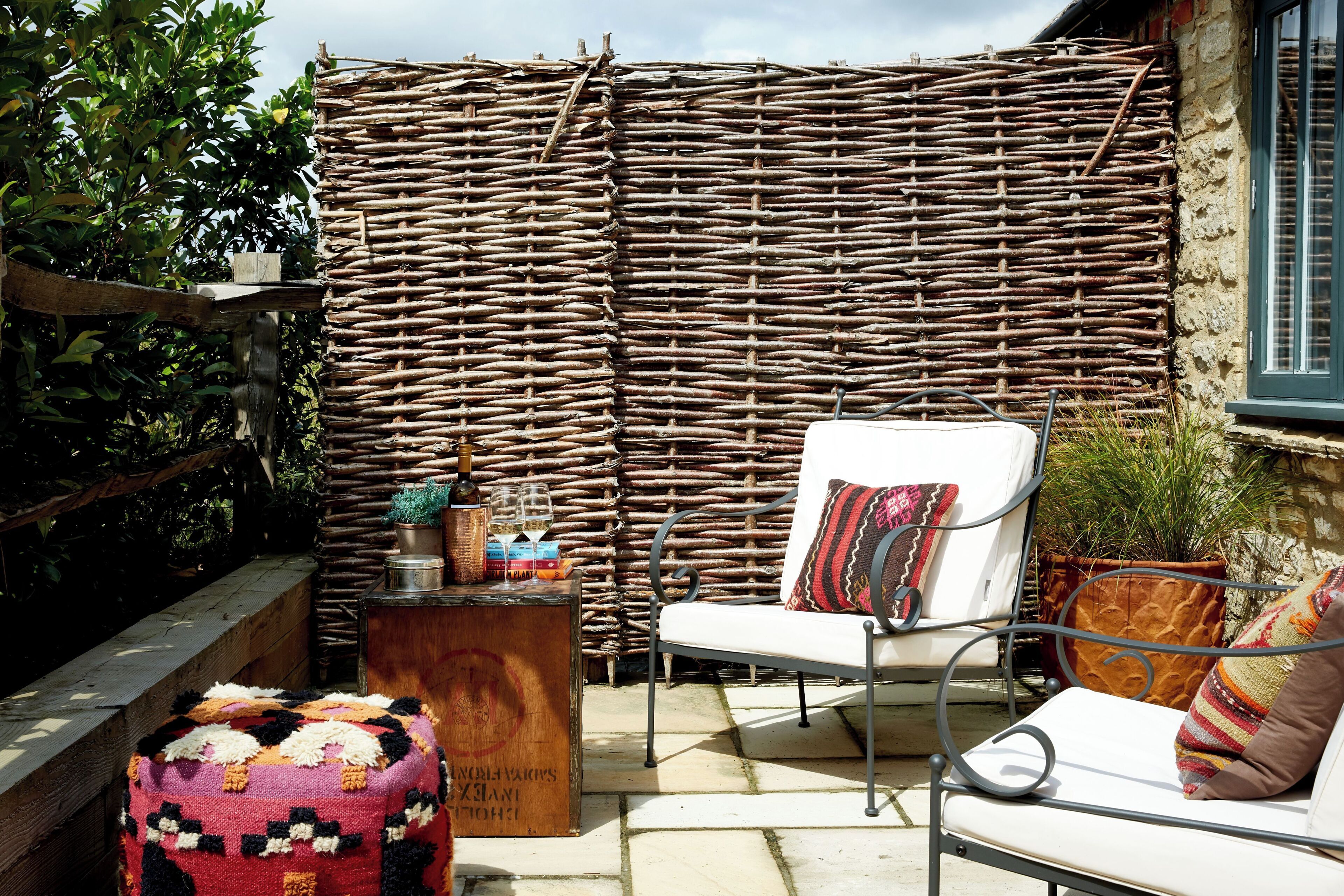 A wicker wall, a white chair, a small table with books and a bottle, and a colorful cushion.