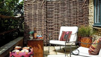 A wicker wall, a white chair, a small table with books and a bottle, and a colorful cushion.