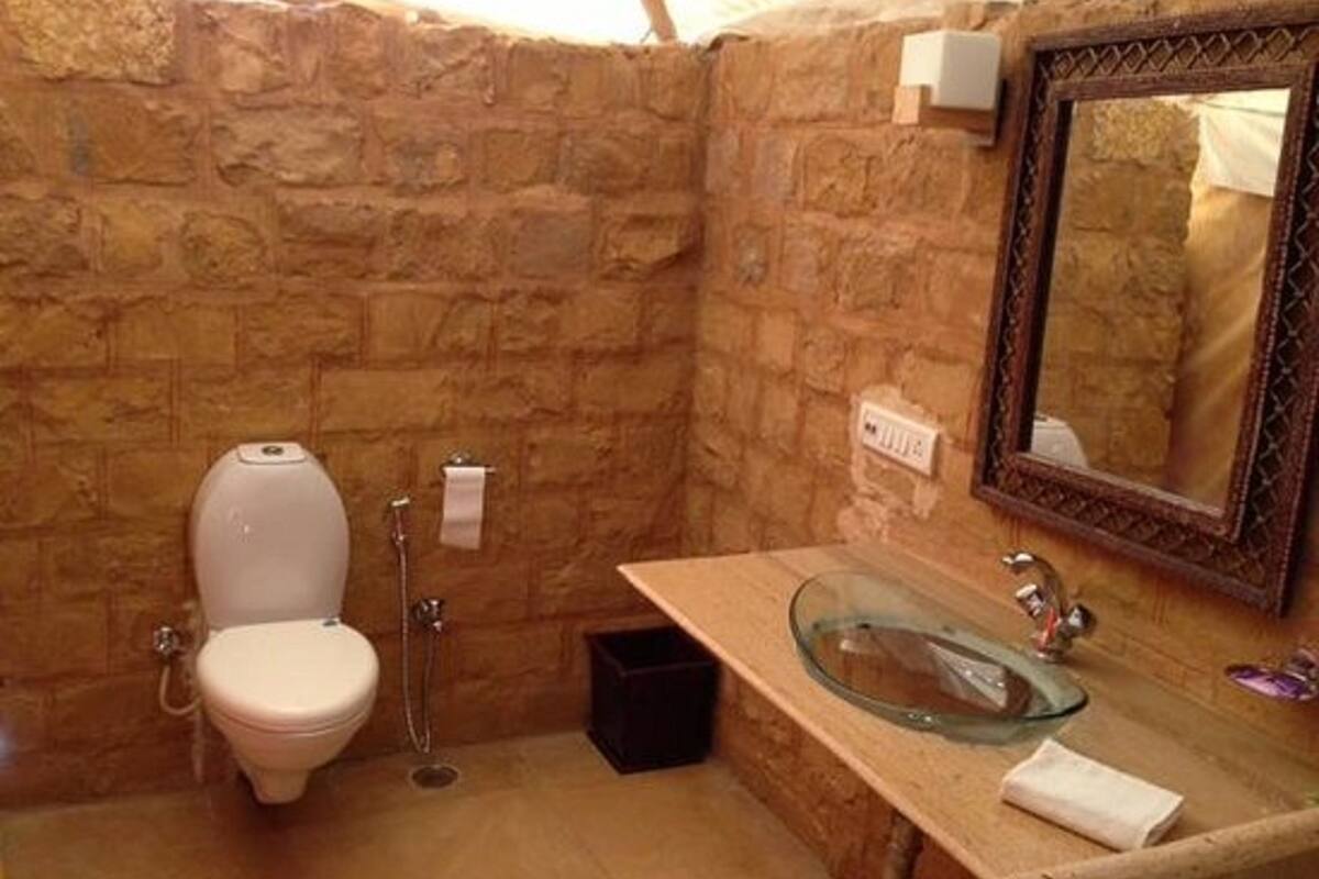 A bathroom with a stone wall, a toilet, a glass sink, and a mirror.