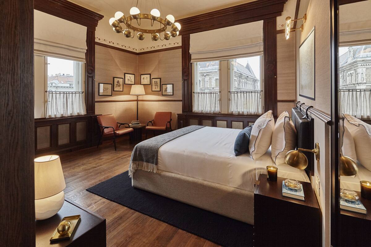 Habitación de hotel con una cama grande, un escritorio, una silla, una lámpara y cuadros en la pared.