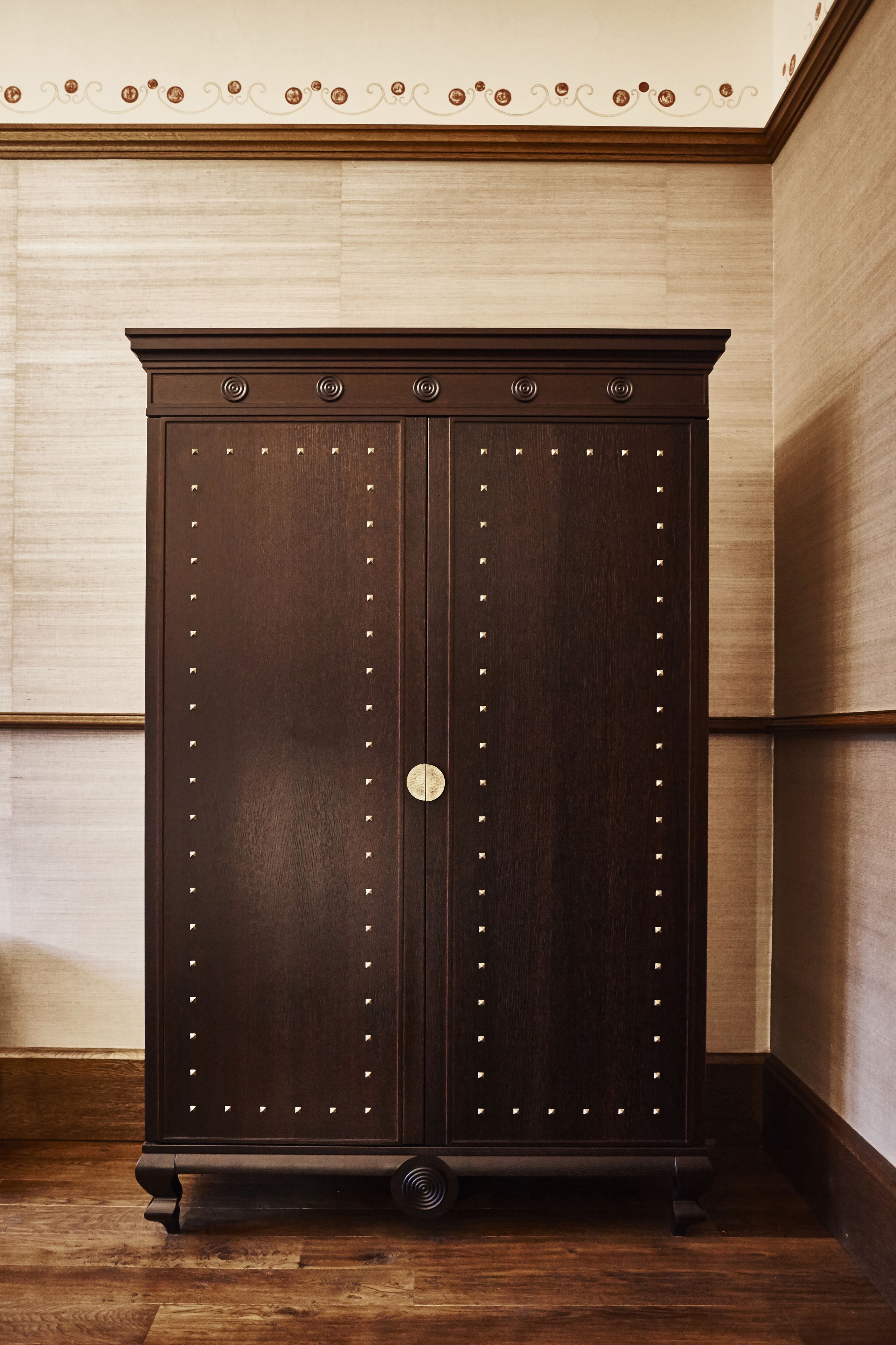 A dark wooden wardrobe with a circular handle and decorative studs.