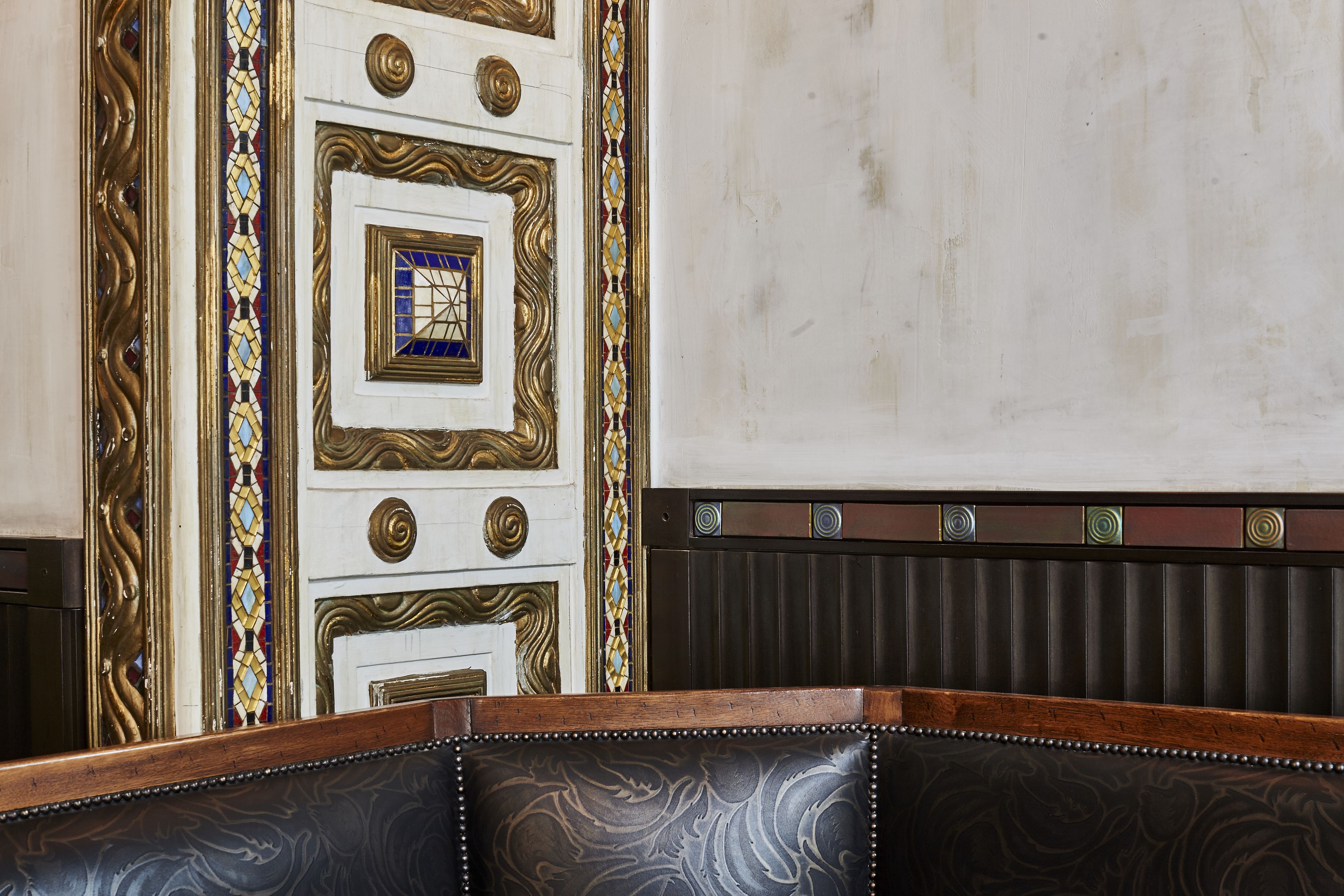 Una habitación con decoraciones ornamentales en las paredes, un banco tapizado con motivos y un radiador.