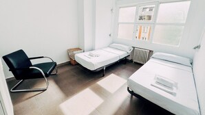 Une chambre avec deux lits simples, une chaise, un radiateur et une fenêtre avec des stores.