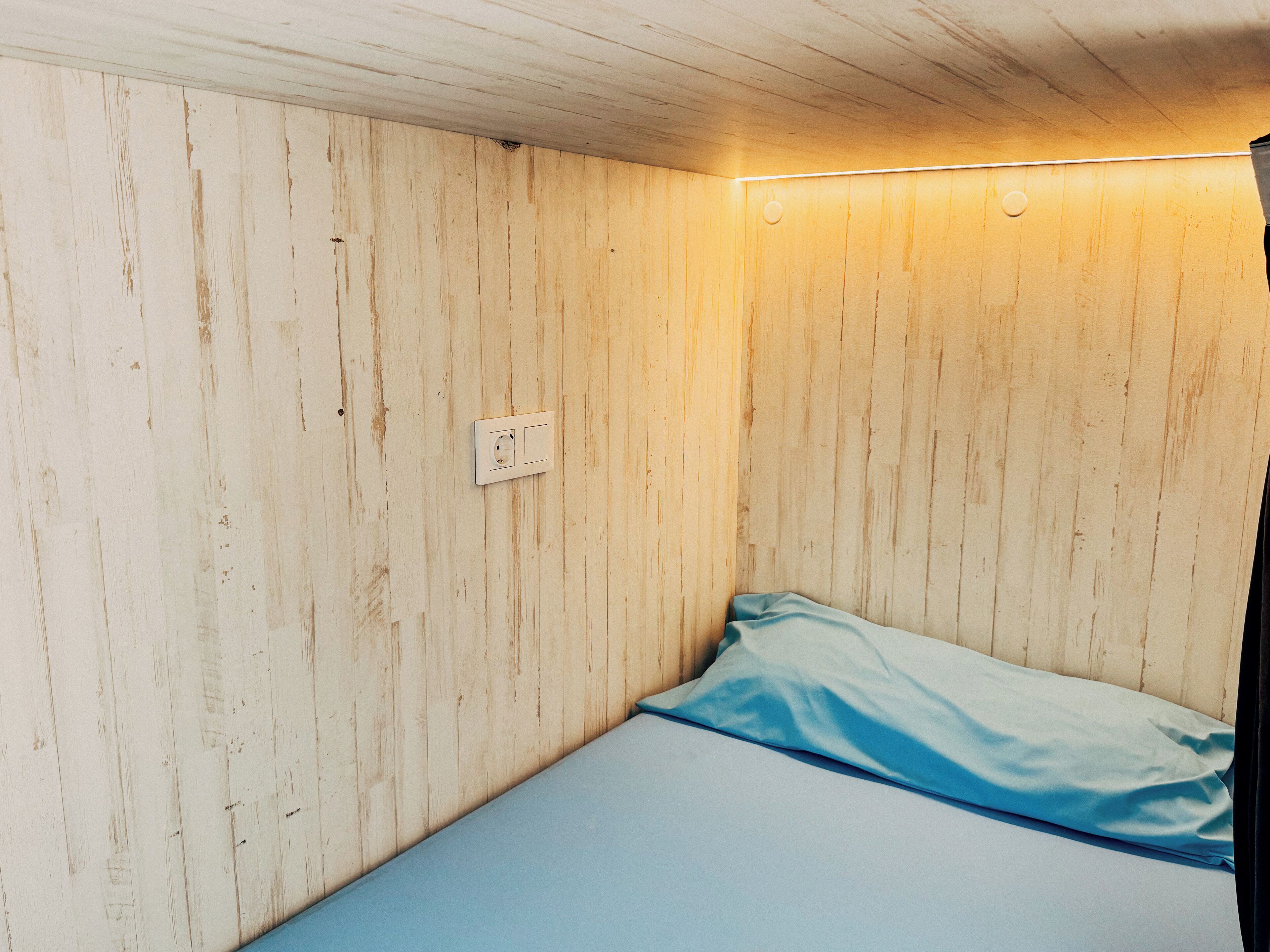 A small, single-bed room with wooden walls and a simple, unadorned ceiling.