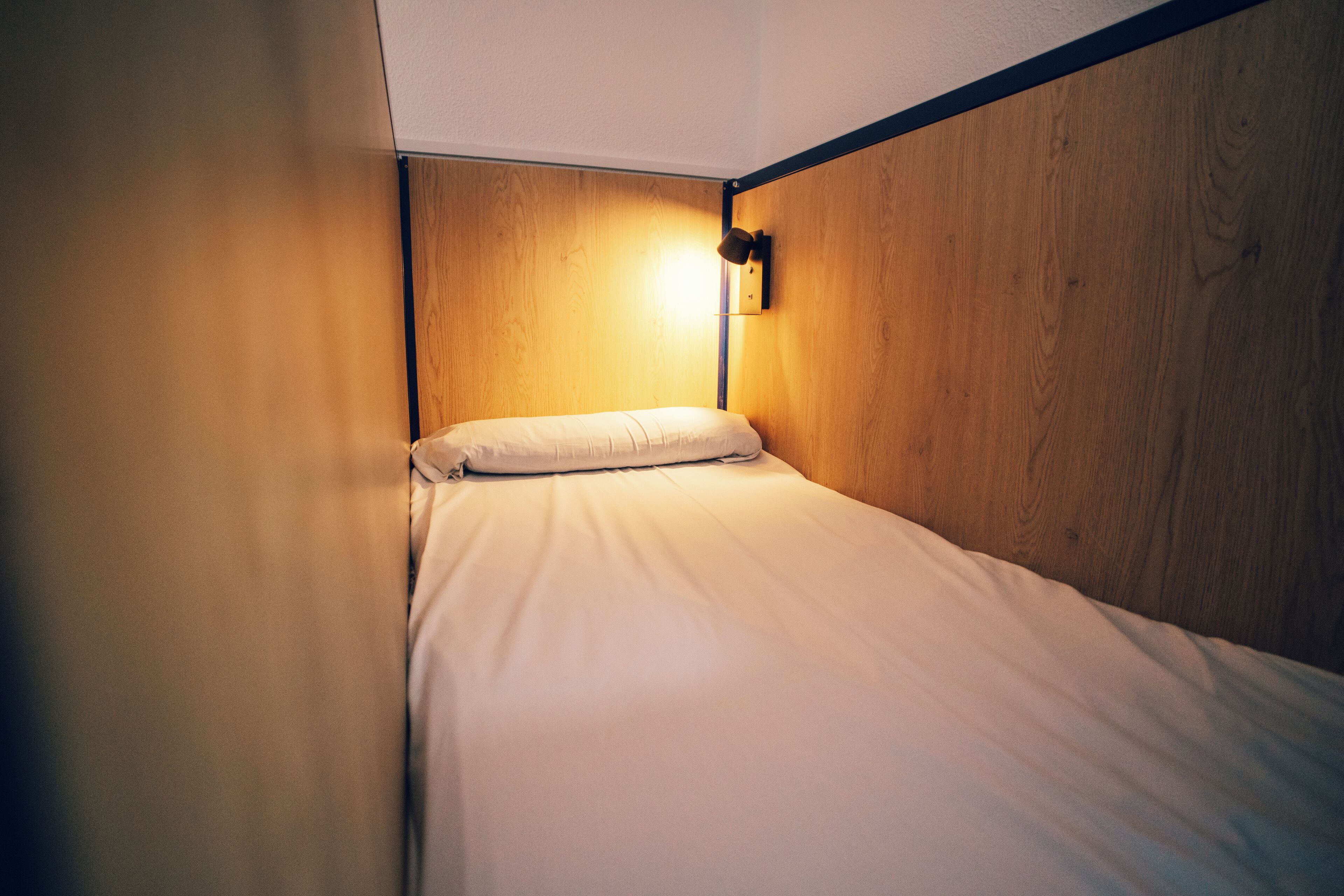 A single bed in a room with wooden walls and a wall-mounted light fixture.