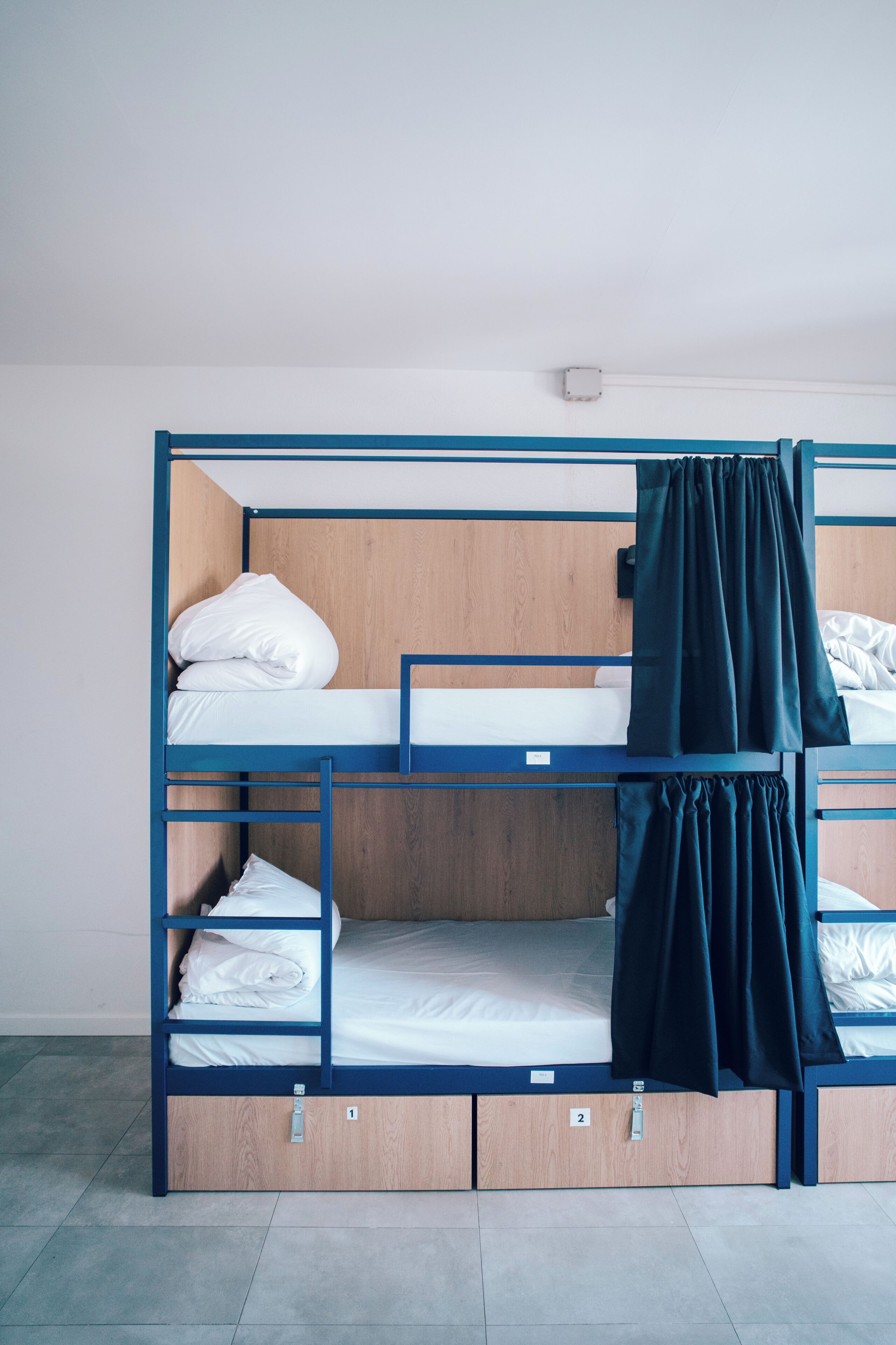 Una cama litera con una base inferior de madera y una superior azul, ambas con ropa de cama blanca.