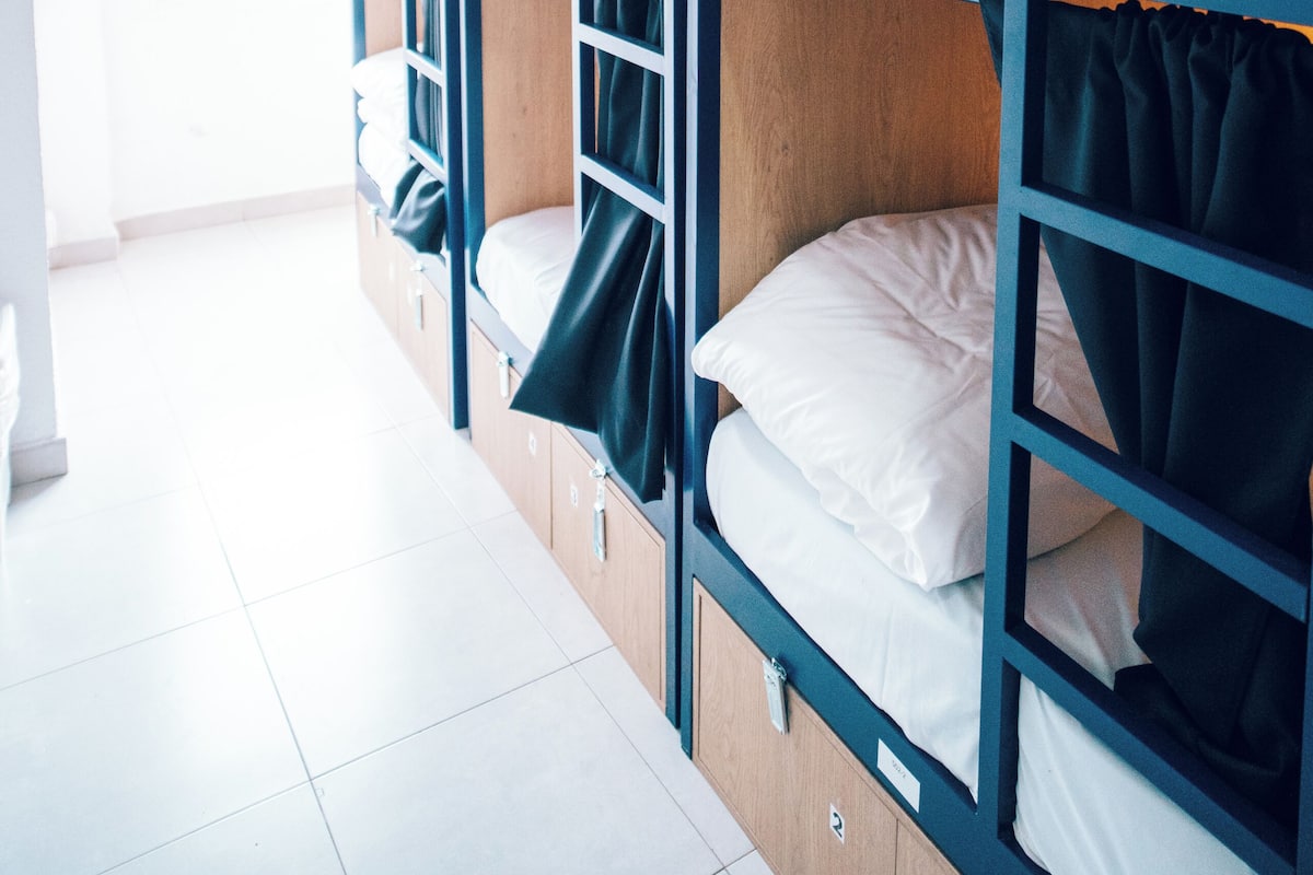 Quarto com beliche de madeira, roupa de cama branca e cortinas escuras.
