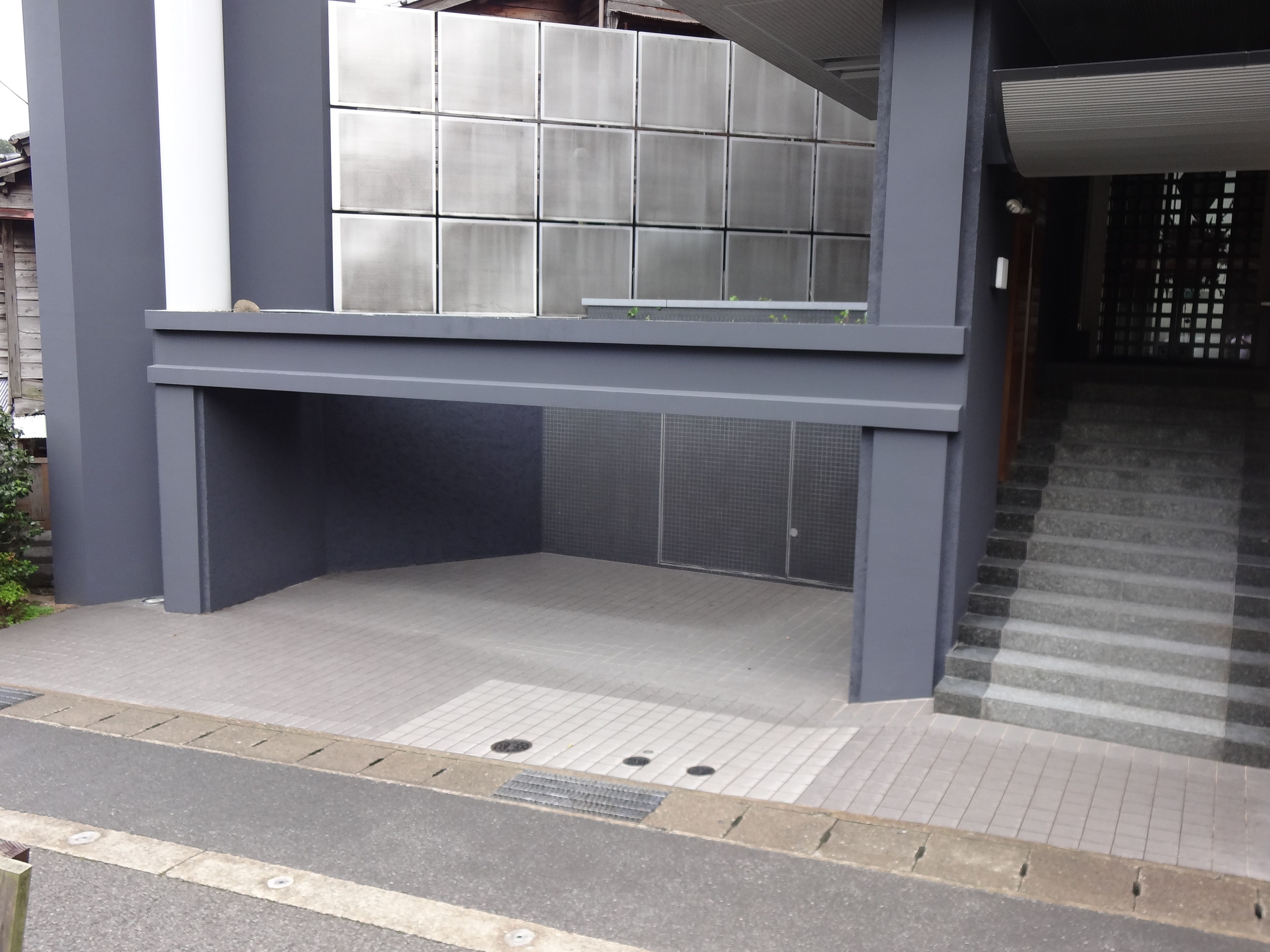 Ein modernes Gebäude mit grauem Fassadenschmuck, einem gefliesten Eingangsbereich und einer Treppe, die nach innen führt.