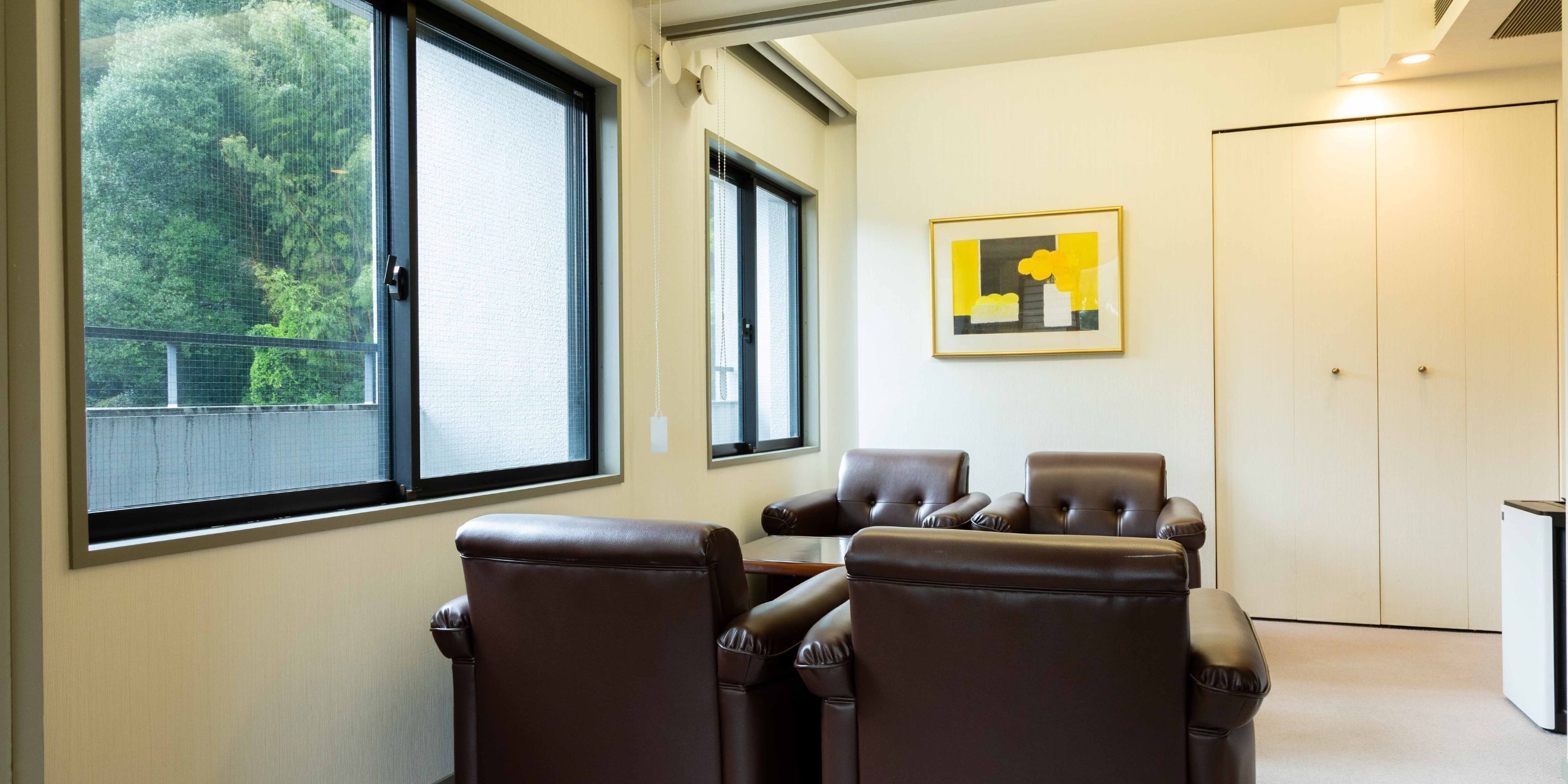 Un salón de conferencias con sillones de cuero, ventanas amplias y un cuadro abstracto enmarcado en la pared.