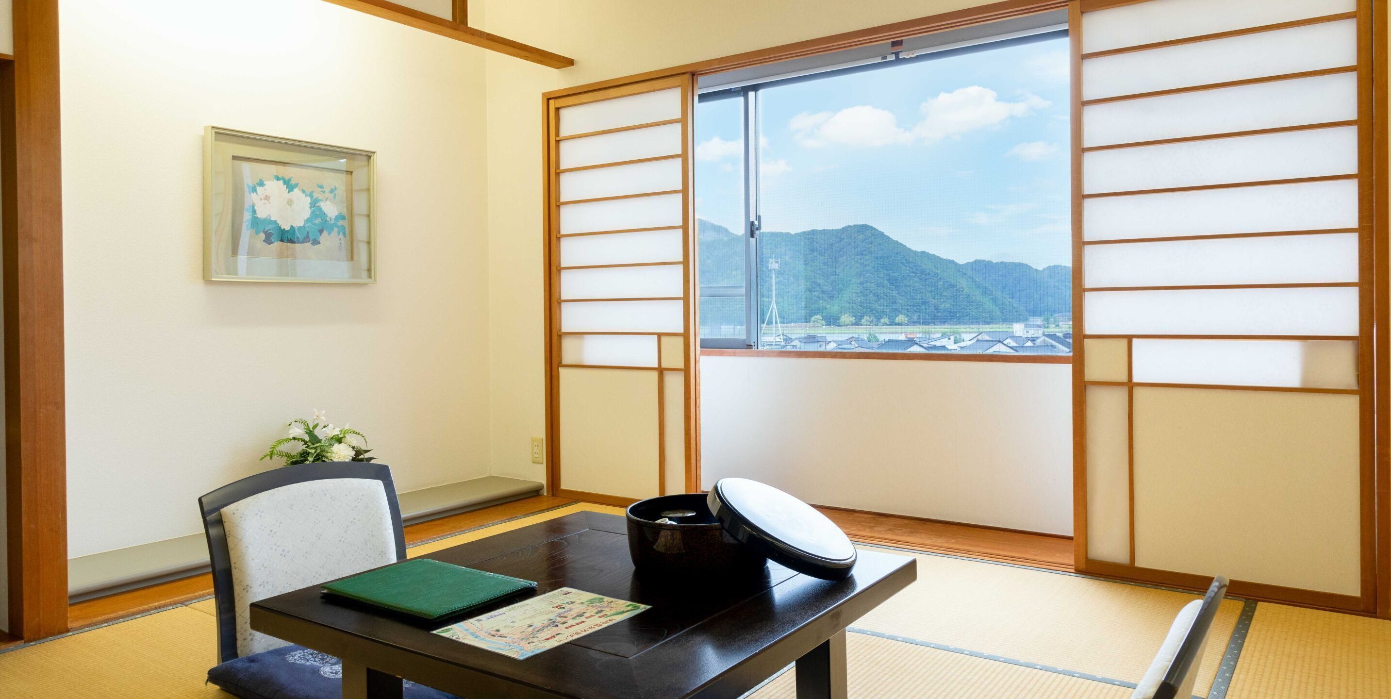 A traditional Japanese room with tatami flooring, a sliding shoji screen, a table with a black kettle, a green folder, and a framed picture on the wall.