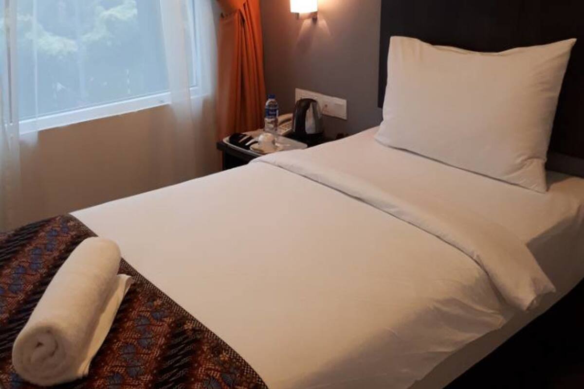 Une chambre d’hôtel avec un lit, une table de chevet, une lampe et une fenêtre avec des rideaux.