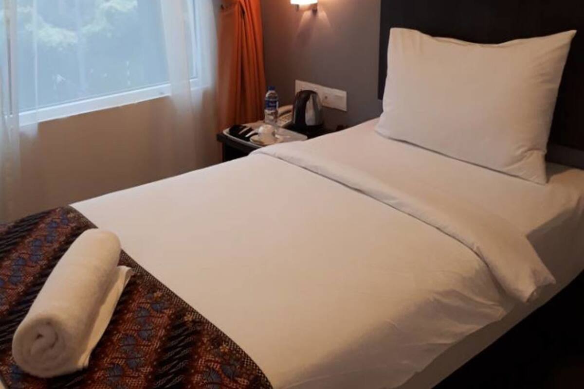 Une chambre d’hôtel avec un lit, une table de chevet, une lampe fixée au mur, une fenêtre avec des rideaux et une citation inspirante sur le mur.