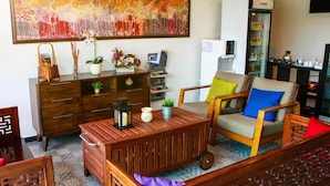 Ein Wohnzimmer mit Couch, bunte Kissen, einem Holztisch, einem Bücherregal, einem Fernseher und einem großen abstrakten Gemälde an der Wand.