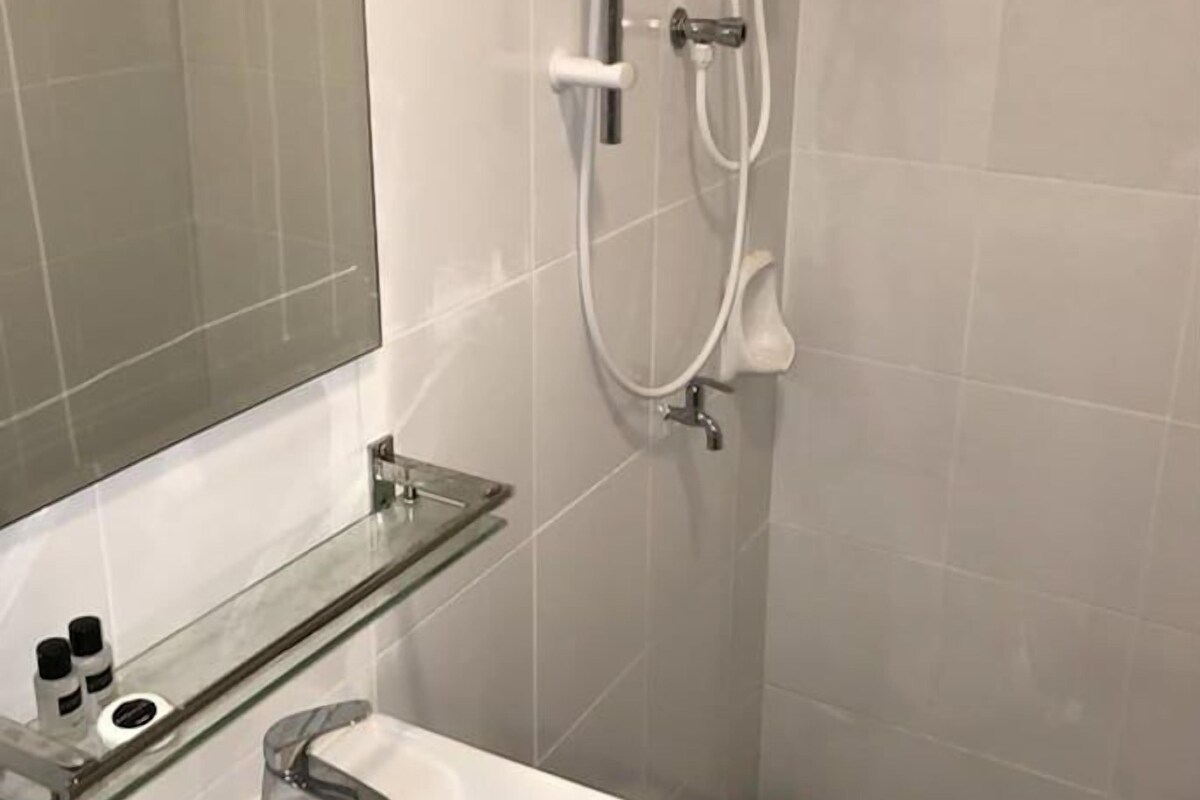 Ein Badezimmer mit einem weißen Waschbecken, einer Glasablage für Toilettenartikel, einer Handbrause und einem karierten Boden.