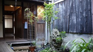 Um jardim japonês tradicional com um deck de madeira, uma planta de bambu, uma formação rochosa e um vaso com planta.