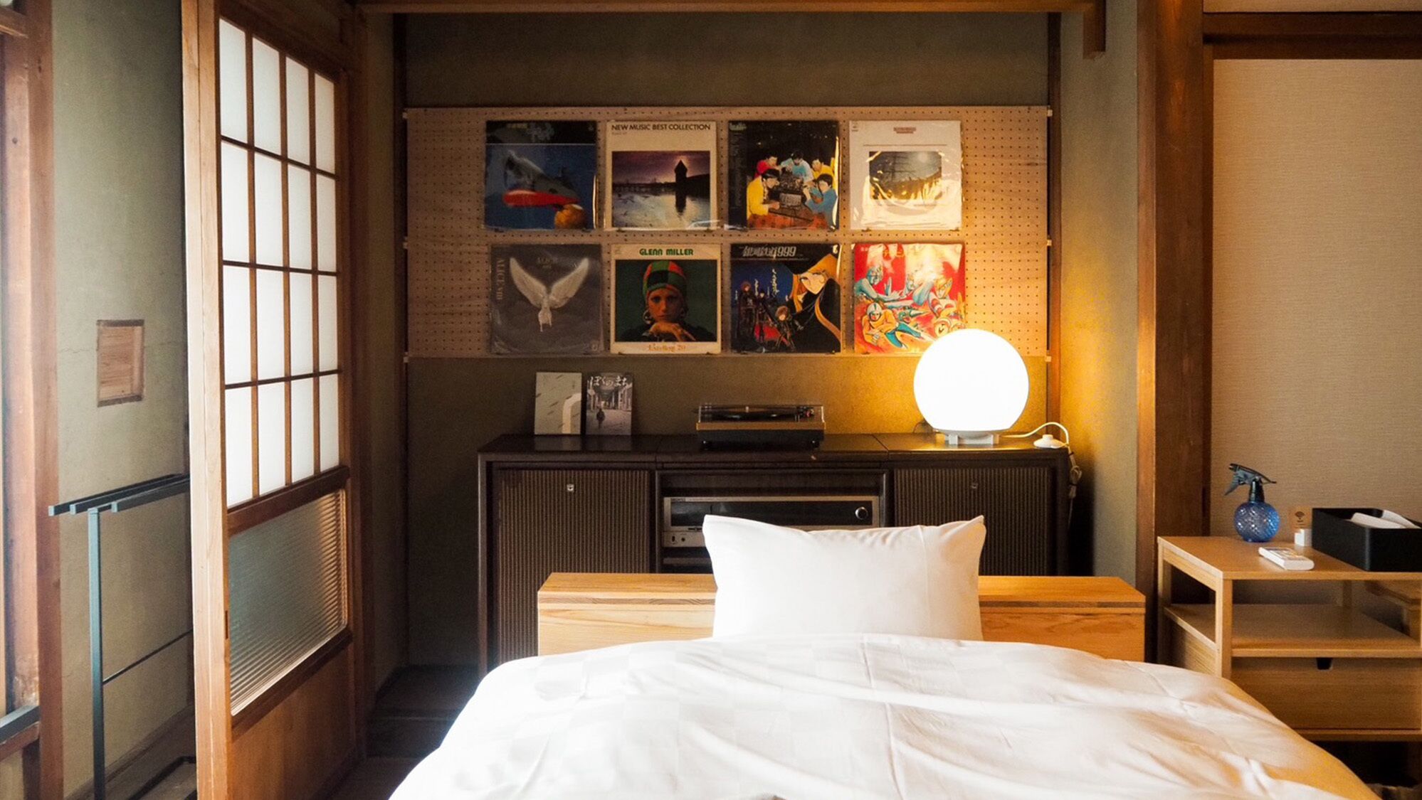 A hotel room with a bed, a desk with a lamp, a pegboard with various items, and a window with blinds.