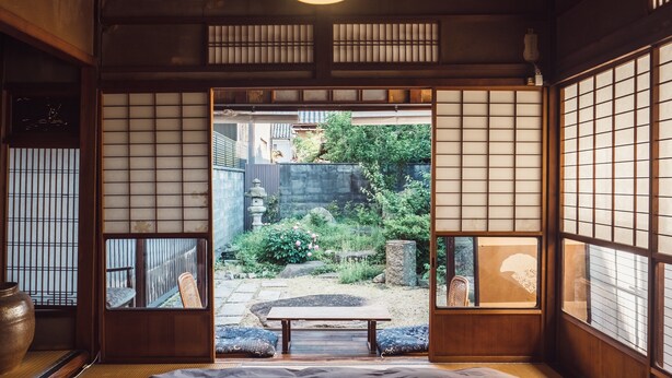 Um quarto japonês tradicional com tatames, painéis shoji e vista para um jardim.