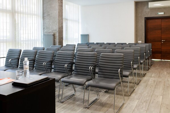 A conference room with rows of black chairs, a table with a laptop and water bottle, and large windows with blinds. - Taurus City (Lviv)