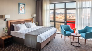 A hotel room with a large bed, two chairs, a small table, and a view of a cityscape. - Taurus City (Lviv)