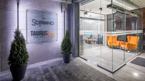 A modern hotel entrance with a glass facade, potted plants, and orange seating inside. - Taurus City (Lviv)