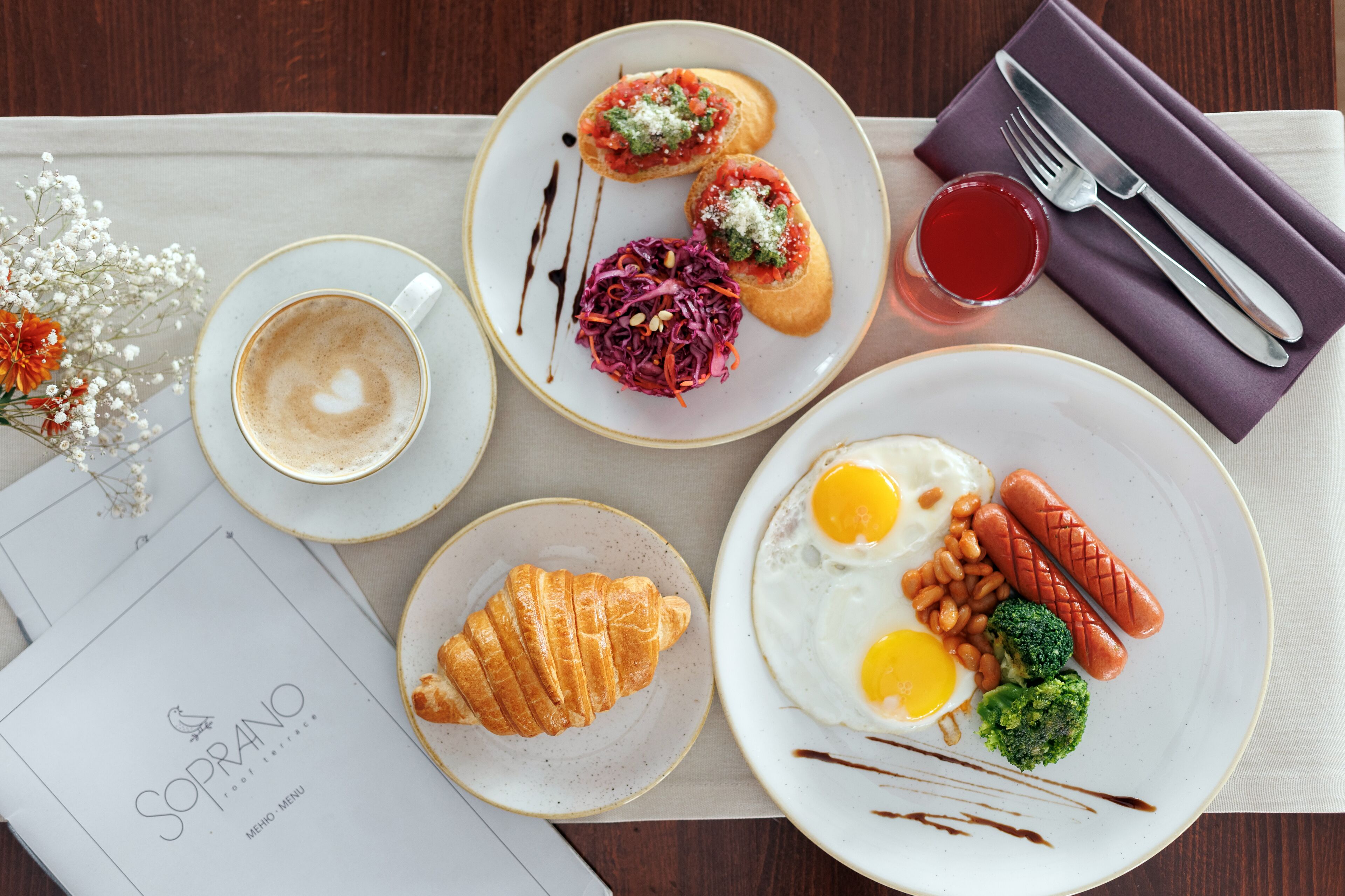 A breakfast setting with croissants, eggs, sausages, and a cup of coffee on a table.