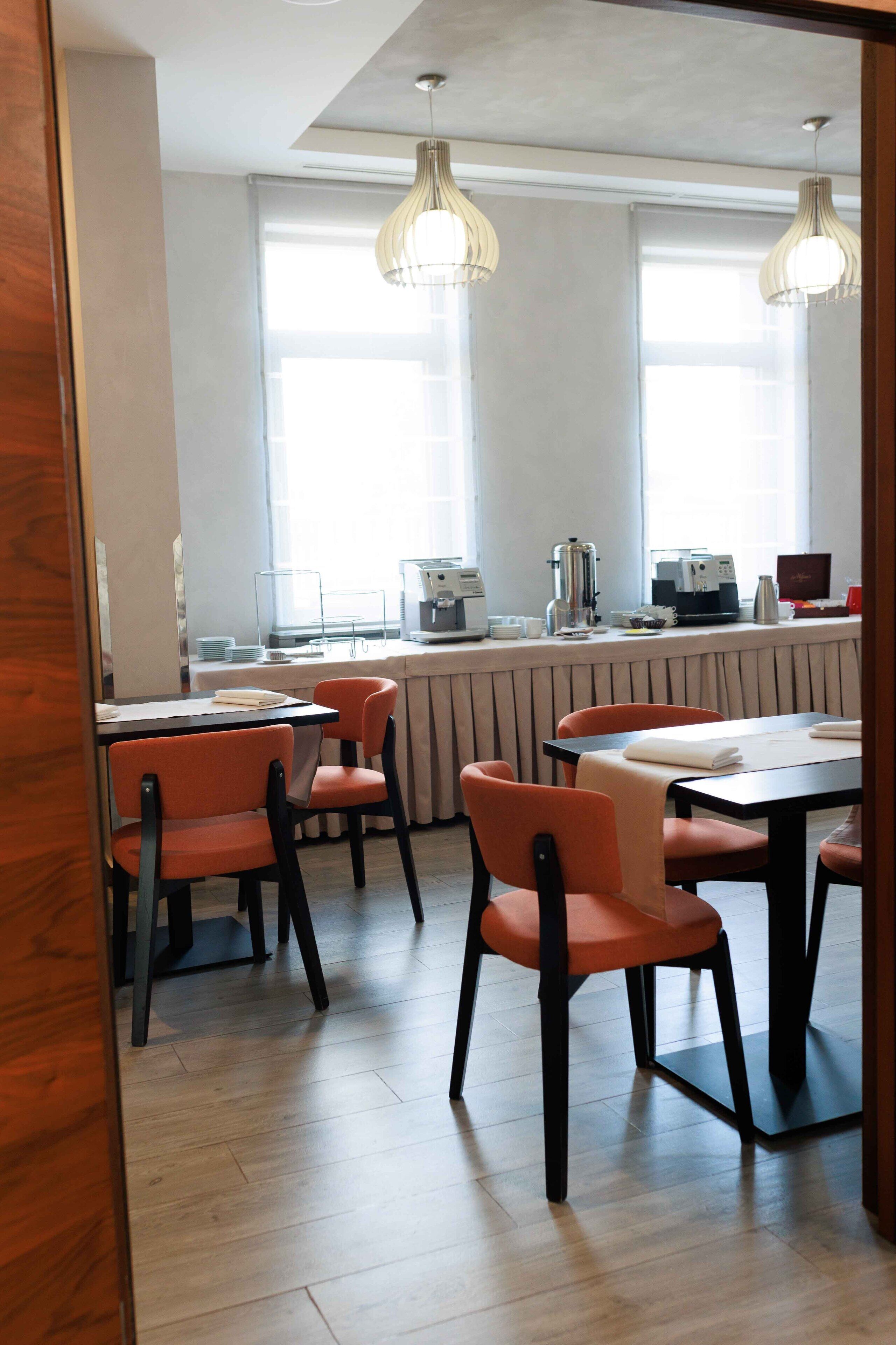 A modern dining area with wooden flooring, orange chairs, and a counter with coffee machines.