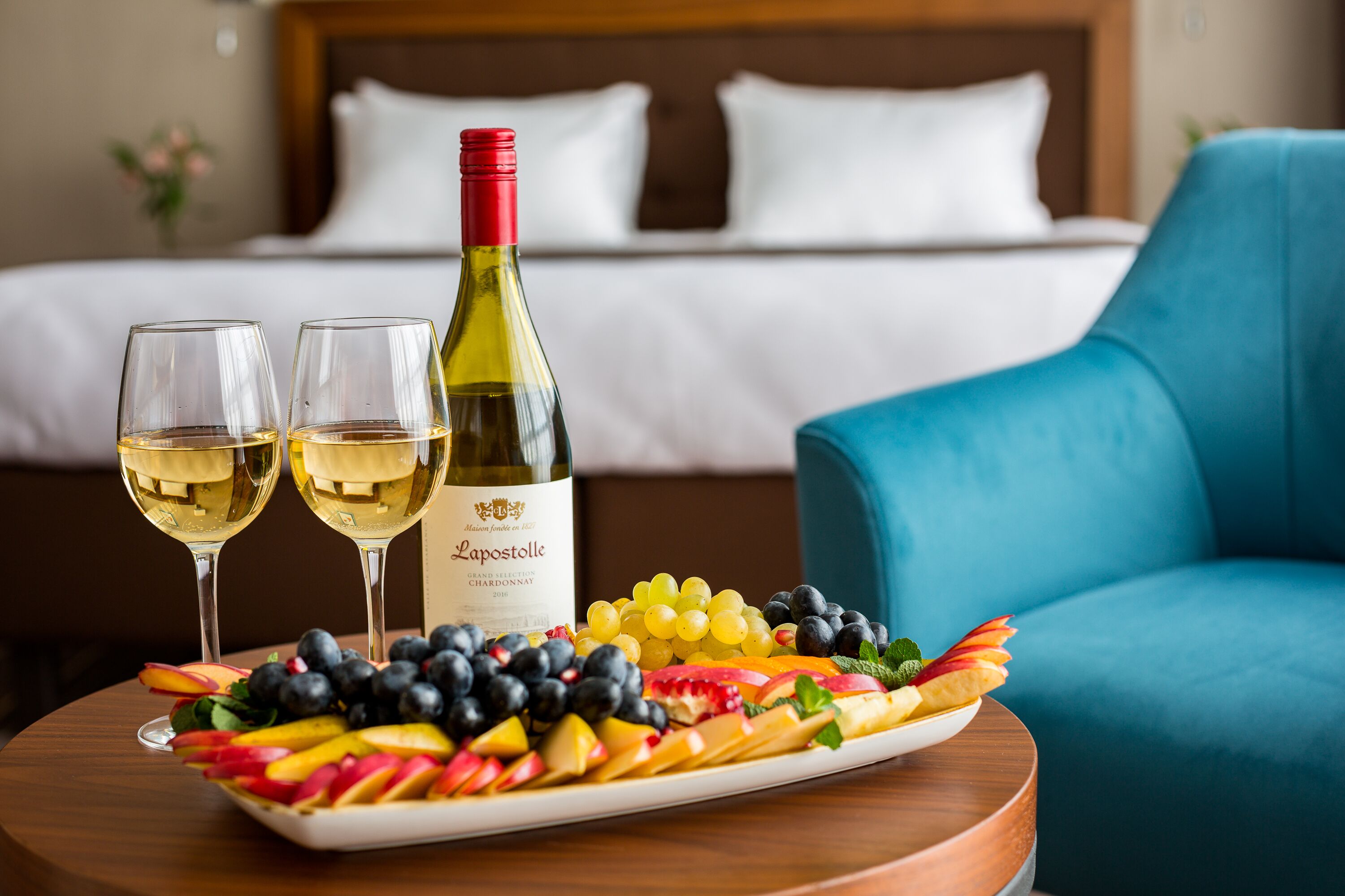 A dining table with a wine bottle, two glasses of white wine, and a fruit platter.