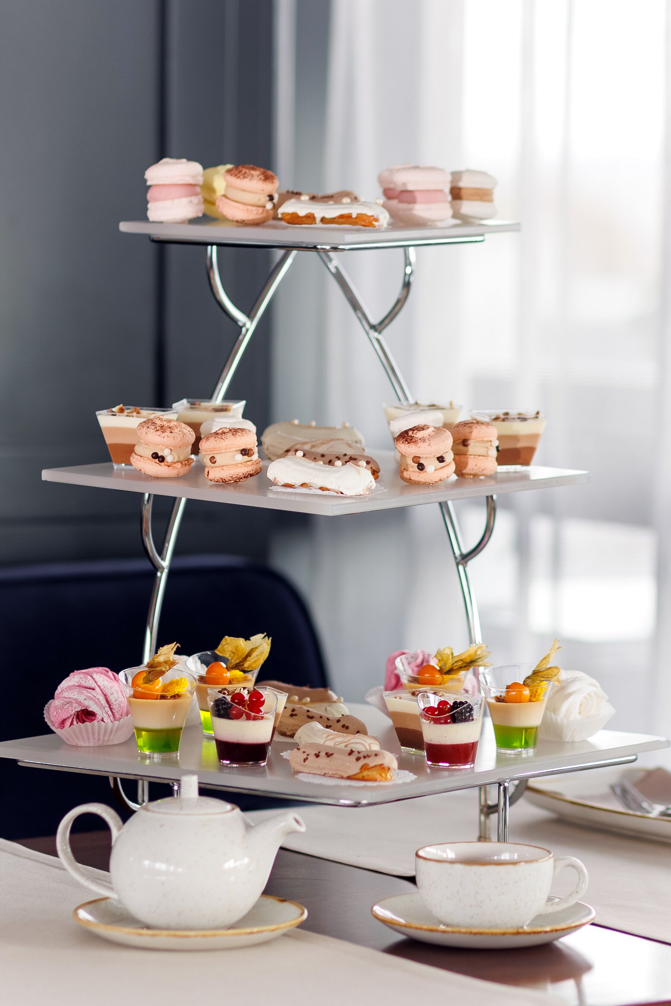 Een etagère met diverse gebakjes en desserts, een theepot en een kopje op een tafel.
