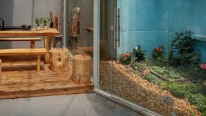 A room with a wooden table, benches, a hanging light fixture, and a glass enclosure with plants. - Bushe Cuoguo Inn (Xiamen)