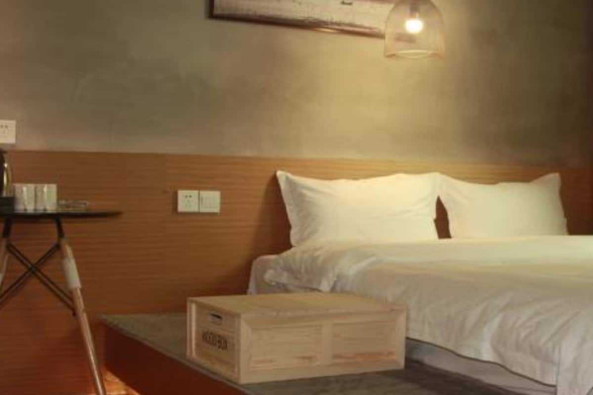 A bedroom with a wooden headboard, a bed with white bedding, a small table with a lamp, and a box on the floor.