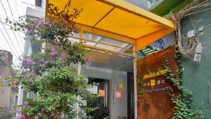 A building entrance with a covered porch, a potted plant, and a sign with Chinese characters. - Bushe Cuoguo Inn (Xiamen)
