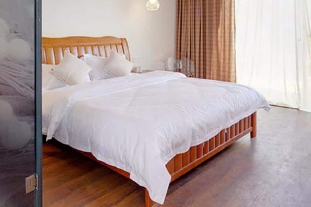 A bedroom with a wooden bed, white bedding, a nightstand, and a window with curtains.