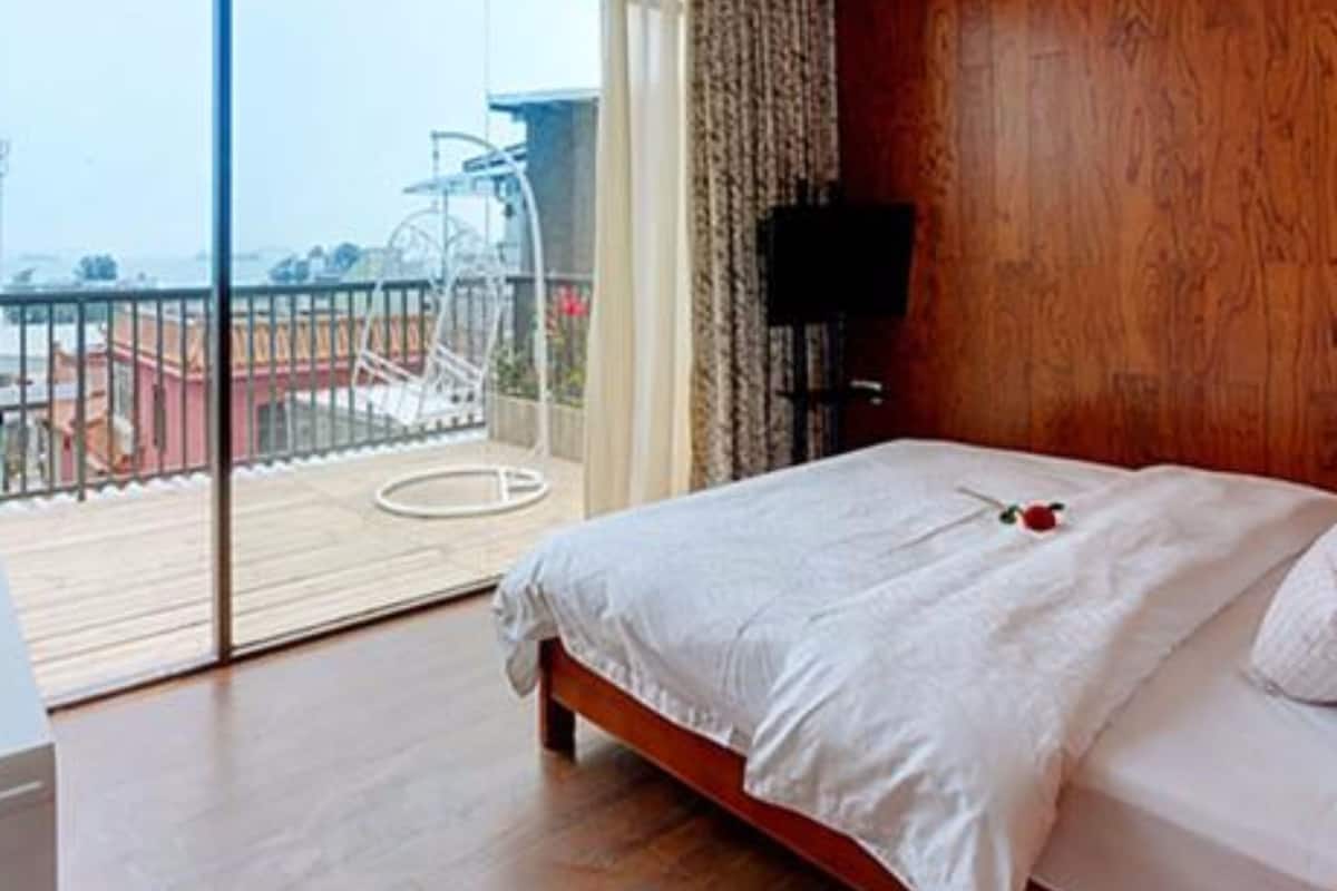 A bedroom with a large window, a wooden floor, and a bed with white bedding.