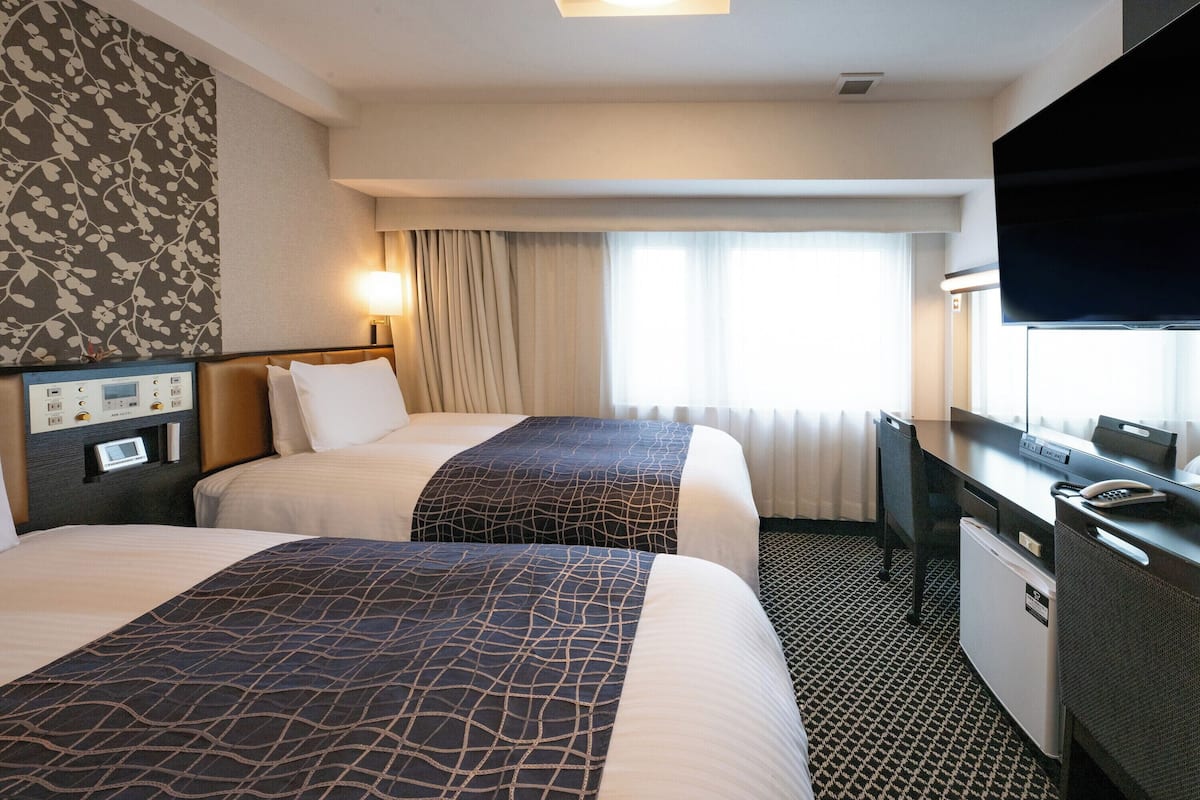 A hotel room with two beds, a desk with a TV, and a minibar.