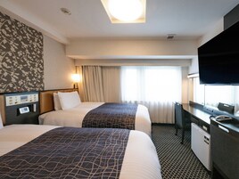 A hotel room with two beds, a desk with a TV, and a minibar.
