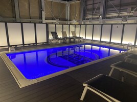 Una piscina interior con una fuente iluminada en azul, rodeada de sillones de descanso y una terraza de madera.