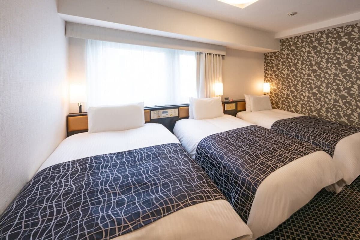 Habitación de hotel con dos camas, una ventana con cortinas, un muro con estampado floral y lámparas de noche.