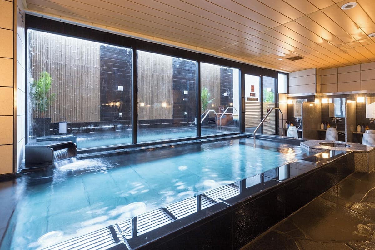 A spa area with a large indoor pool, wooden ceiling, and a view of a bamboo fence outside.