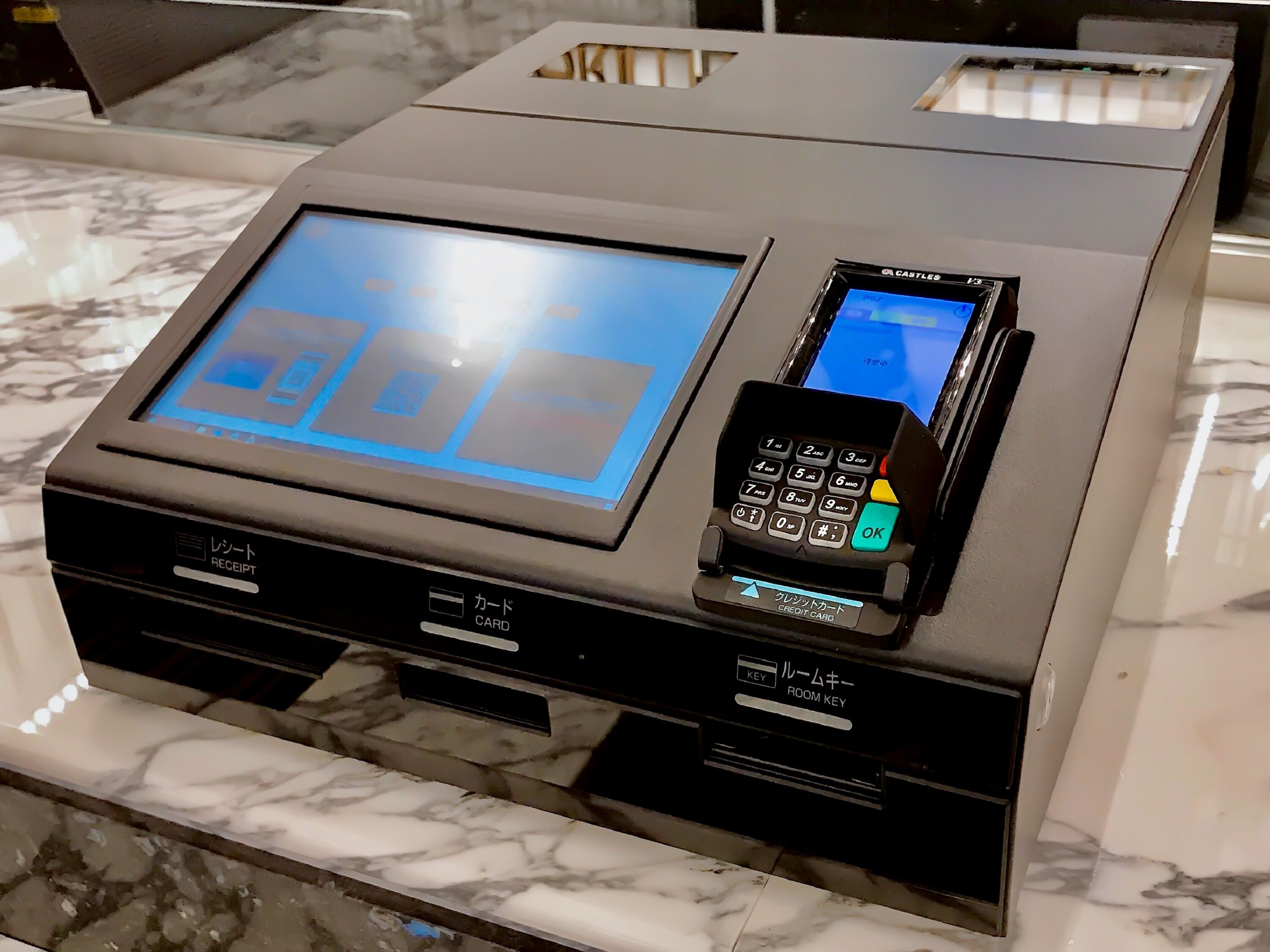 Mostrador de recepción de hotel con pantalla digital, lector de tarjetas y estación para llaves de habitación.
