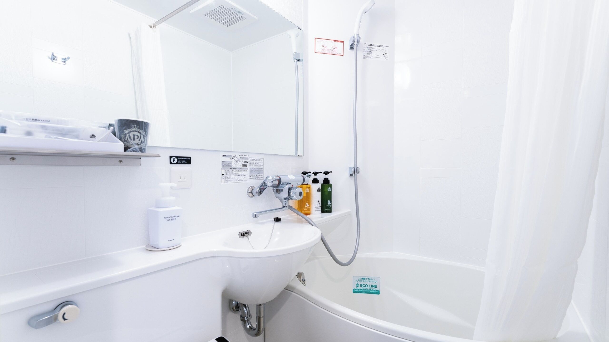 Un bagno moderno con un lavandino bianco, uno specchio, una doccia e una vasca da bagno. Sul lavandino ci sono articoli da toilette e un cartello che indica le caratteristiche ecologiche del bagno.