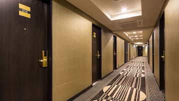 A hotel corridor with doors marked with room numbers, a patterned carpet, and a ceiling with recessed lighting.