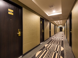 Ein Hotelgang mit Türen, die mit Zimmernummern gekennzeichnet sind, einem gemusterten Teppich und einer Decke mit eingelassenen Leuchten.