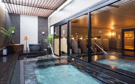 A modern indoor pool area with a wooden ceiling, large windows, and a seating area with a hot tub.