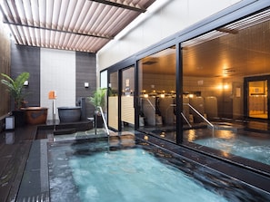 Un área de piscina interior moderna con techo de madera, ventanas amplias y zona de estar con hidromasaje.