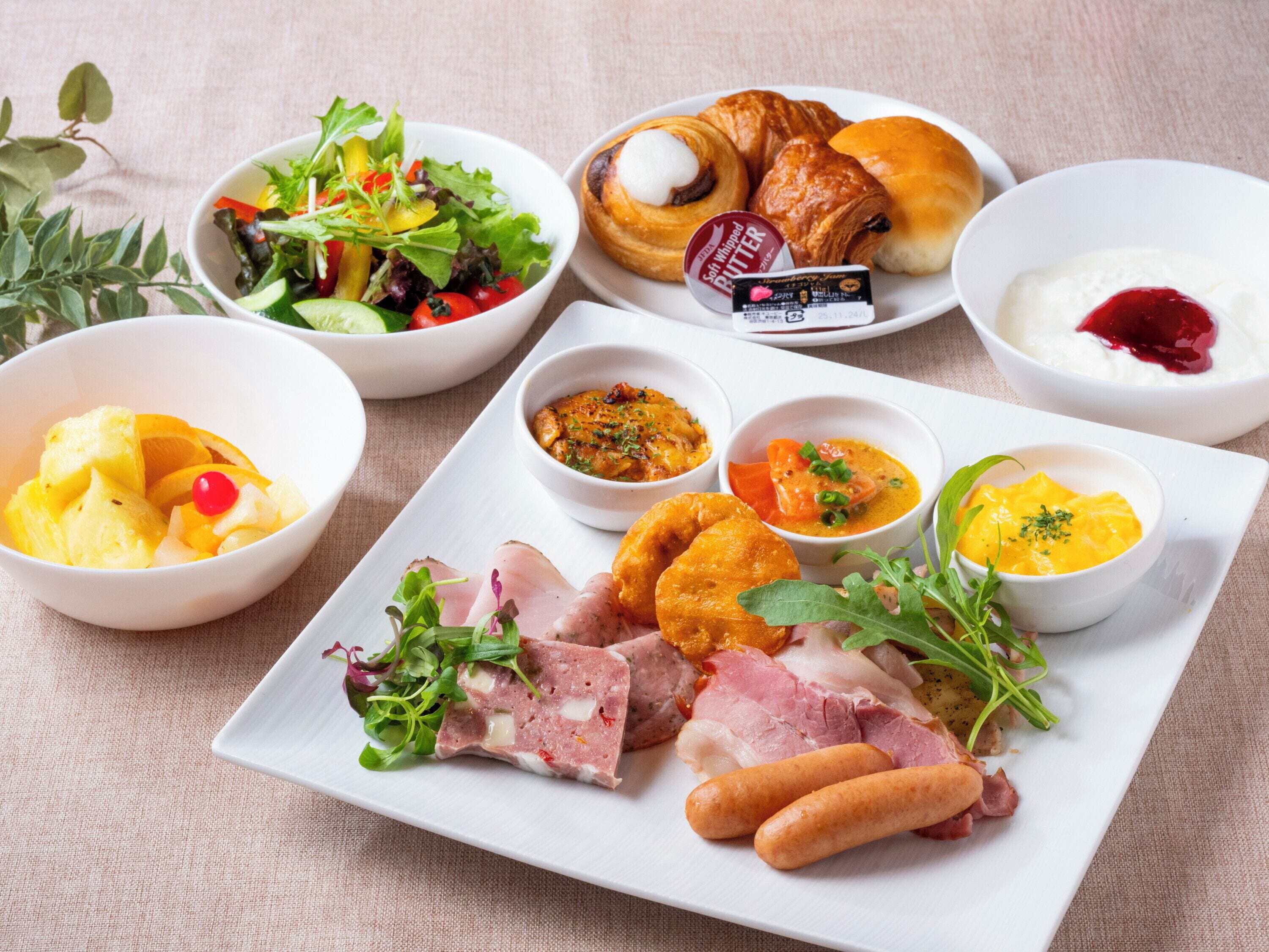 A variety of dishes including a salad, croissants, and meat.