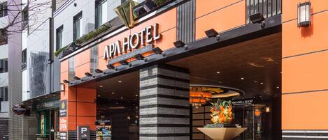 Exterior del APA Hotel & Resort, con un diseño moderno, que presenta una entrada destacada, un arreglo floral y un letrero con el nombre del hotel.