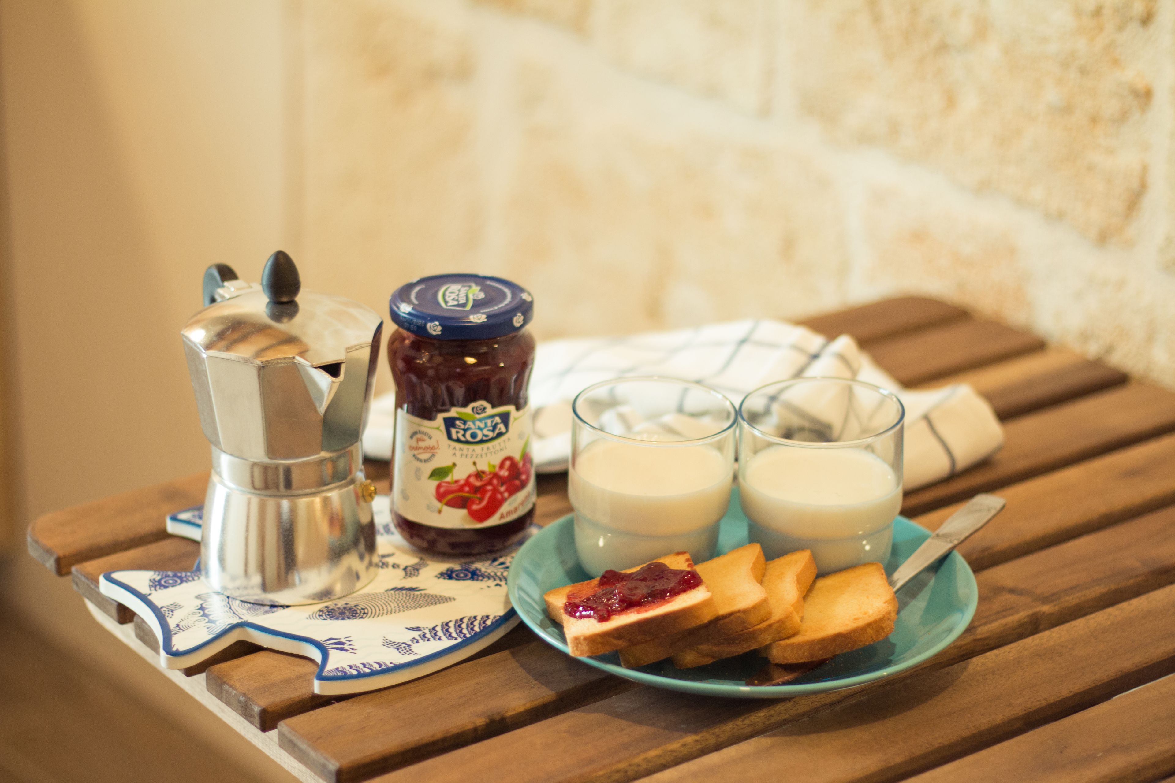 Et bord med en kaffemaskine, et syltetøjsglas, to glas mælk og ristet brød med syltetøj på en blå tallerken.